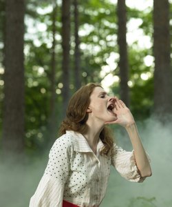 Woman in old-fashioned dress in forest, holding hand to mouth and calling