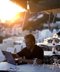 Man using laptop computer at outdoor cafe at sunset