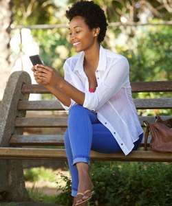 Young lady relaxing a park bench and using mobile phone