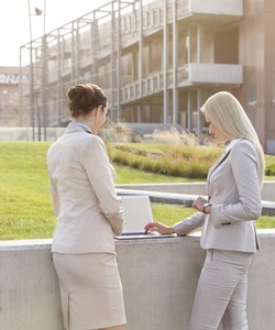 Young businesswomen working together on laptop while standing against office building