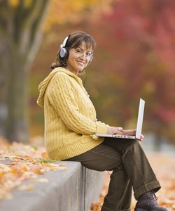 Hispanic woman using laptop outdoors with headphones