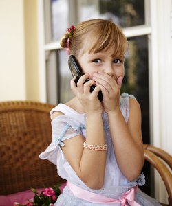 Girl (6-7) using mobile phone, covering mouth with hand