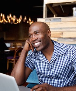 Happy african man sitting at a cafe with laptop