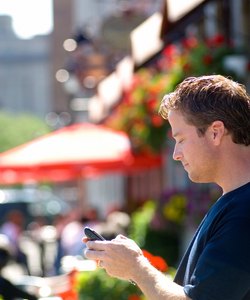 Man using cellular PDA in front of summer street cafe.