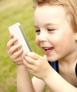 Boy holding white cell phone in park, smiling