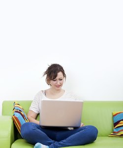 Full length of happy young woman using laptop while sitting on green sofa