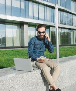 Young businessman in sunglasses with coffe laptop talking phone
