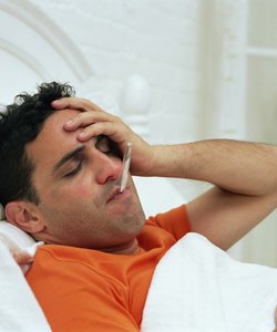 Man in bed with thermometer in mouth, holding head, eyes closed