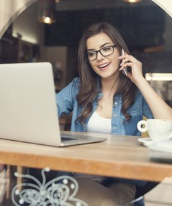 Woman talking by mobile phone and using laptop at cafe