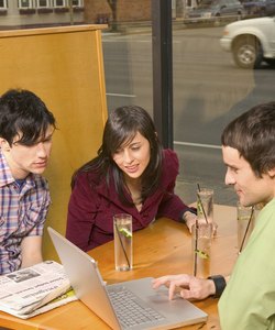 Caucasian Twenty Somethings Sitting In An Internet Cafe And Laughing While Looking At A Laptop Computer