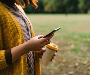 A red-haired woman is walking in the park and holding a bamboo cup with hot coffee