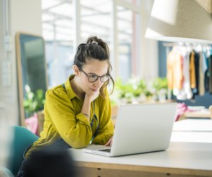Fashion designer sitting at desk in her studio looking at laptop