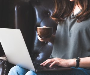 Closeup image of a woman working , using and typing on laptop keyboard while drinking coffee