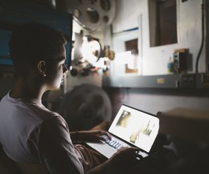 Mixed race tween boy projectionist using laptop in dark movie theater