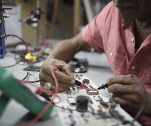 Close up male engineer using soldering iron on electronics