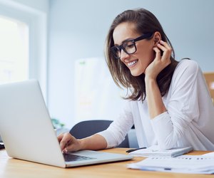 Portrait of beautiful cheerful young businesswoman working on laptop and laughing in home office