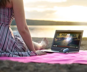 Young woman streaming a movie with laptop computer on beach at sunset. Watching film stream on imaginary online service outdoors. Video player on screen.