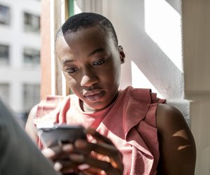 Serious young woman in window sill using cell phone