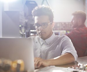 Serious, focused young male designer working at laptop in workshop