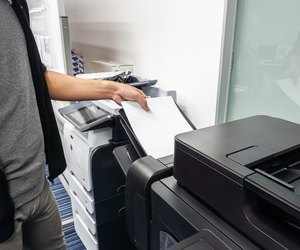 businessman put paper sheet into office printer tray for printing documents