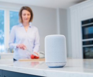 Woman Working In Kitchen With Smart Speaker In Foreground