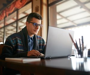 Handsome freelancer businessman working on laptop in cafe. Blogger man updating his profile in social networks with photos sharing with followers multimedia using notebook with wifi. Nerd in glasses