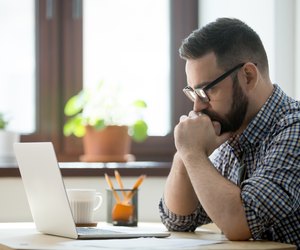 Millennial casual businessman thinking and looking at laptop in office