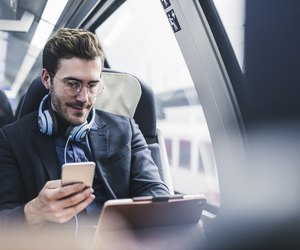 Businessman in train with cell phone, headphones and tablet