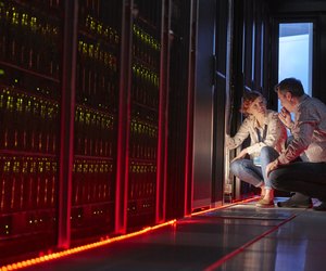 IT technicians talking at glowing panel in dark server room