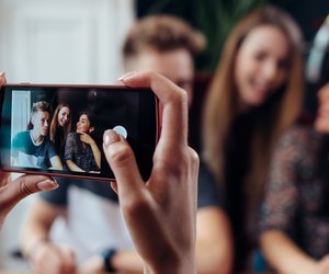 Female hands taking photo with smartphone of young cheerful friends, blurred background