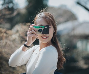 Joyful young woman taking photos with disposable camera in park on a lovely sunny day