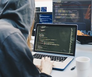 Side view of computer programmer programming on laptop at desk in office