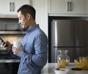 Man drinking coffee and using smart phone in morning kitchen