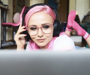 Young woman with pink hair listening to music via laptop at home