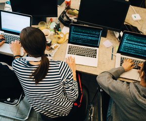 High angle view of young computer programmers coding on laptops at desk in small office