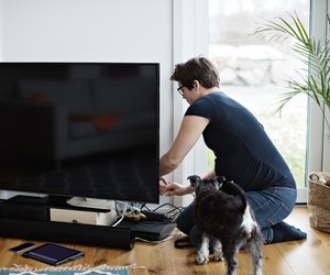Pregnant woman arranging cables of television set while kneeling by dog in living room