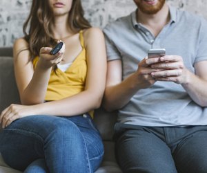 Couple sitting on couch with remote control and smartphone, partial view