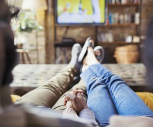 Affectionate couple holding hands, watching TV in living room