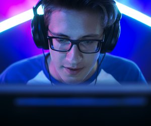 Professional Gamer Plays in MMORPG/ Strategy/ Shooter Video Game on His Computer. He's Participating in Online Cyber Games Tournament, Plays at Home, or in Internet Cafe. He Wears Glasses and Gaming Headphones, Talks into Microphone.
