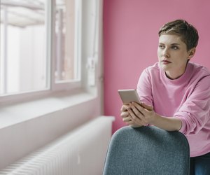 Pensive woman with cell phone looking out of window