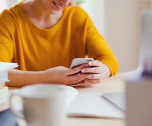 A young female student sitting at the table, using smartpone when studying.