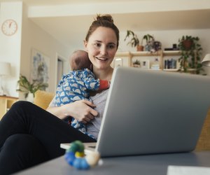Mother using laptop and holding her newborn baby at home