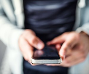 A close-up of unrecognizable young sporty man with smartphone standing in the city.
