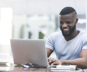 Smiling african man textmessaging on laptop in cafe