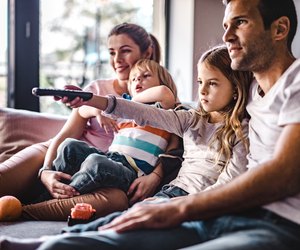 Young parents enjoying with their small kids on sofa while watching TV together.