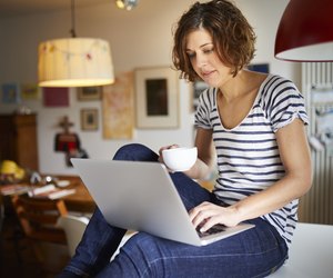 Portrait of mature woman sitting on kitchen table using laptop