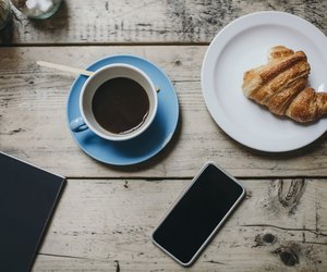 Directly above shot of smart phone with coffee and croissant on wooden table