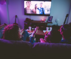 Multi-ethnic teenage friends watching TV together at hangout house