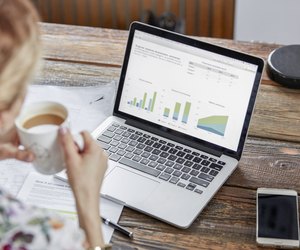 Businesswoman drinking tea and reviewing data at laptop