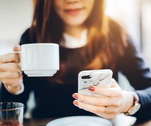 Close up of young woman having coffee and reading news on mobile phone in the early morning before work